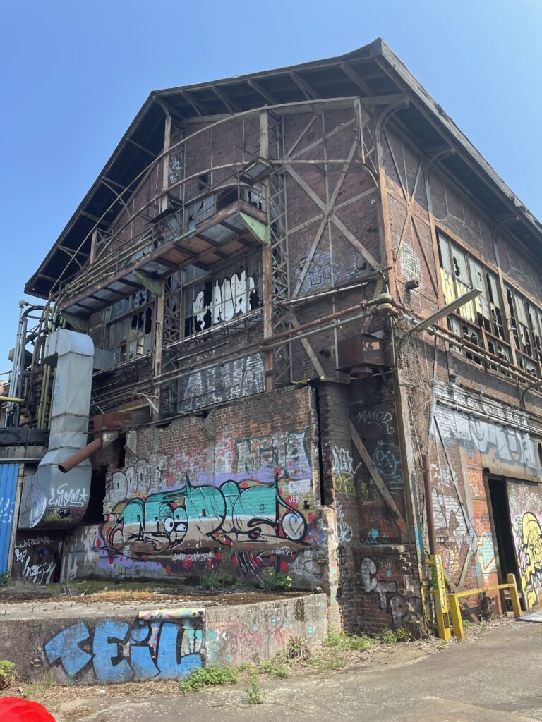 Ansicht einer baufälligen Industriehalle aus dem 19. Jahrhundert. Auf der Außenwand sind viele Graffiti und Tags zu sehen.